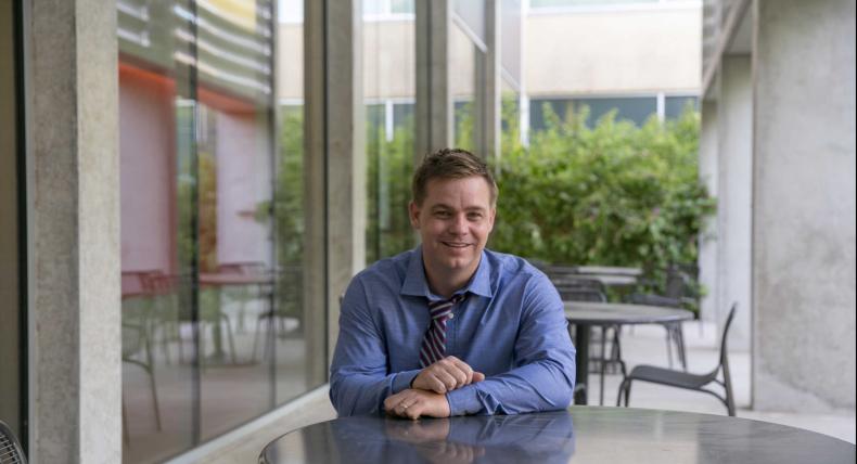 Professor Adam McCormick sits at a patio table outside of Equity Hall.