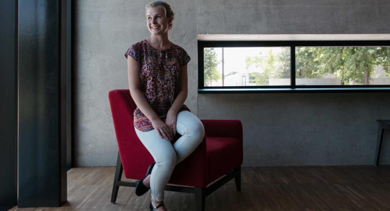 Alma Baker sits on a red chair and looks out the window in the Munday Library.