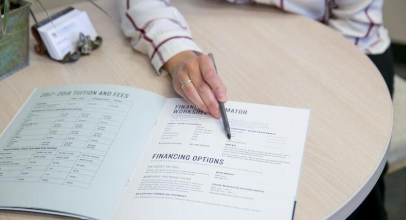 A person pointing at a financial aid pamphlet with a pen