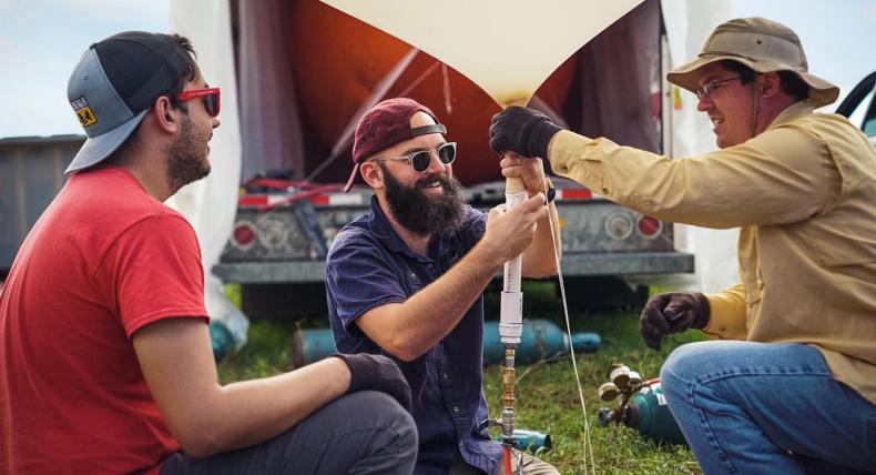 Three researchers kneel and work together to set up a weather balloon.