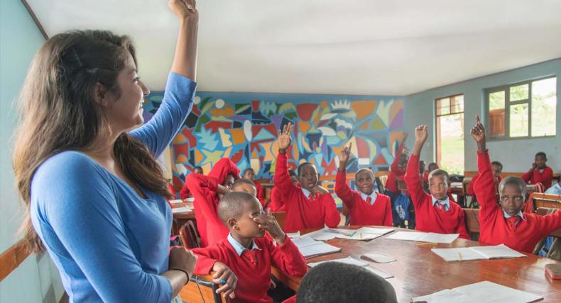 Samantha Mendoza raises her hand as the students she is teaching in Tanzania raise their hands in a classroom.