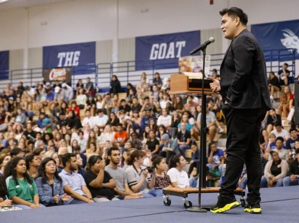 Jose Antonio Vargas stands in front of a podium and microphone and speaks to the audience in the RAC gym.