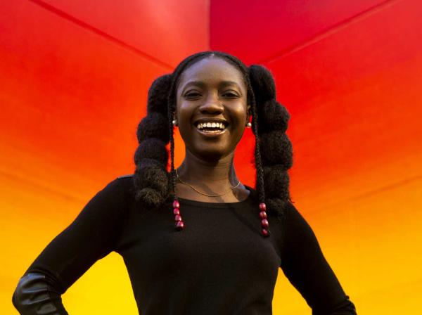 Kadija Samura smiles and stands in front of a warm gradient mural.