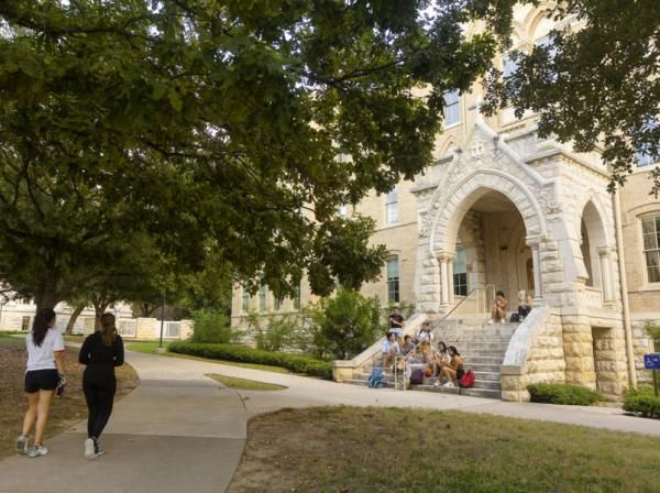 Two students walk on a path as other students sit on the steps of Holy Cross Hall.