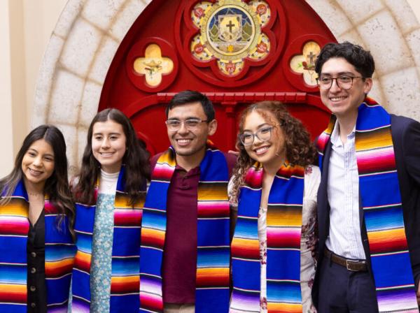 4 students in front of a red door with graduation sashes 