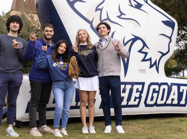 Five students hold up the toppers up hand sign in front of a Fear The Goat inflatable.