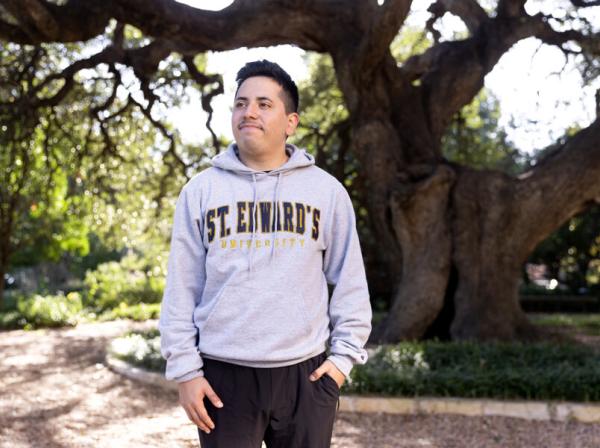 Ethan Tobias wears a St. Edward's hoodie and stands in front of Sorin Oak.