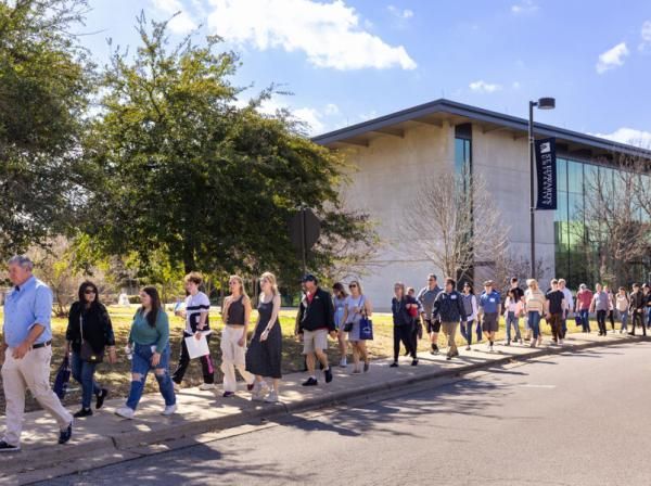 Families participating in a campus tour walk on a sidewalk with Munday Library in the background