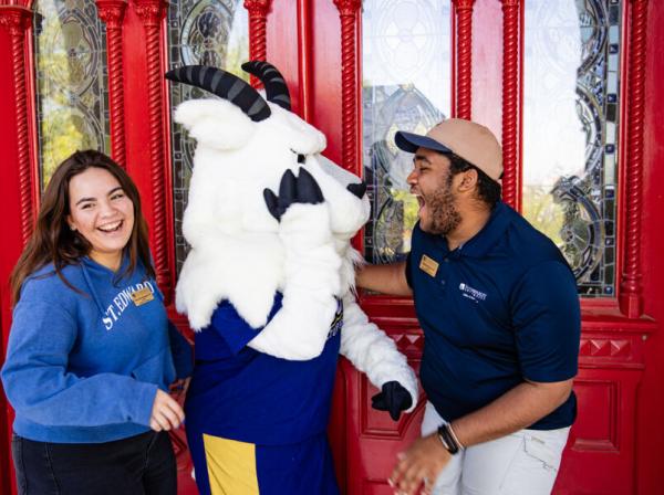 Two students and topper stand and laugh together outside of the red doors.