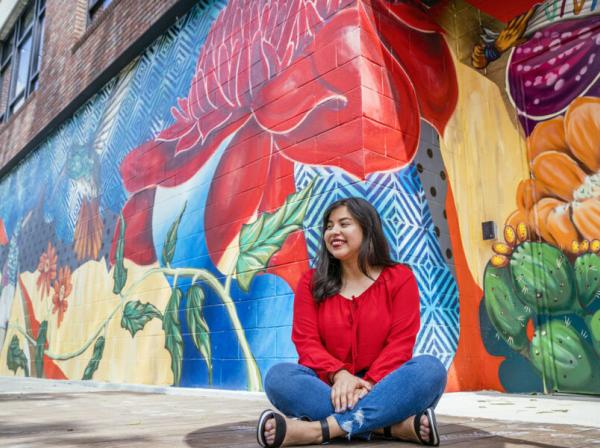 Bianca Esquivel sits in front of a colorful mural.