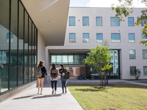 Three students walk on a path by the St. Andre Apartments.