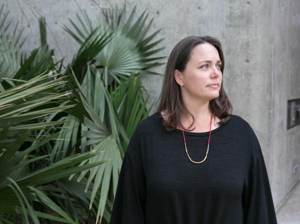 Laurie Cook Heffron stands by tropical greenery and a concrete wall.