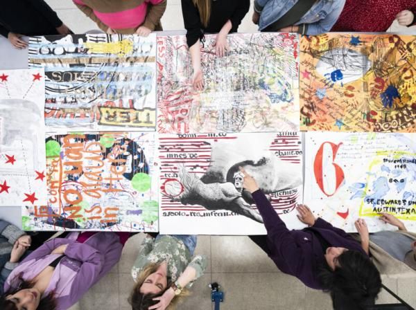 An overhead view of a class looking at and pointing at pieces of artwork.