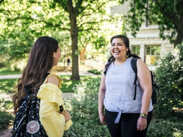 Two students talk outside amongst greenery.