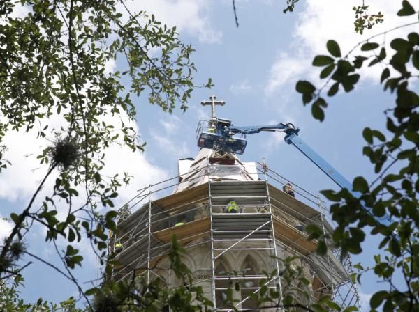 Main Building's steeple under construction, framed by foliage.