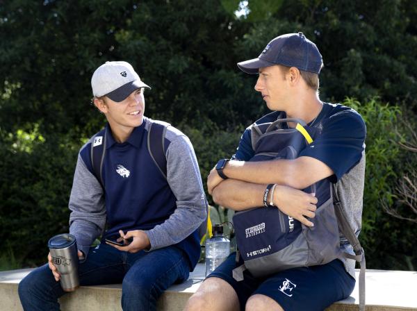 Two students wearing St. Edward's athletic gear sit and chat outside.