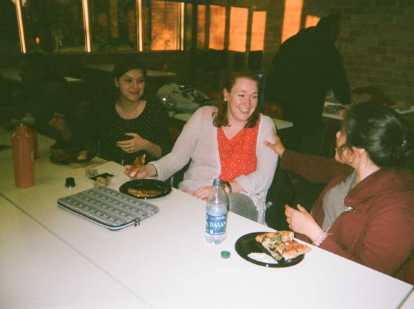 Three students sit at a table with food and talk.