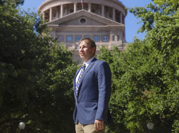 Professor David Thomason stands outside of the Texas State Capitol, framed by trees.