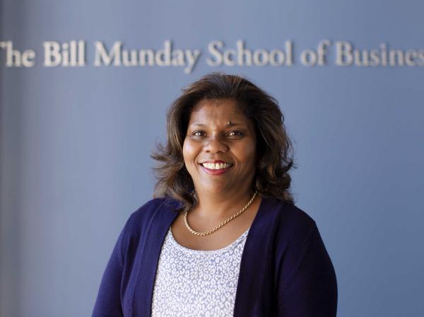 Marianne Ward-Peradoza stands in front of a blue wall that has silver text that reads The Bill Munday School of Business.