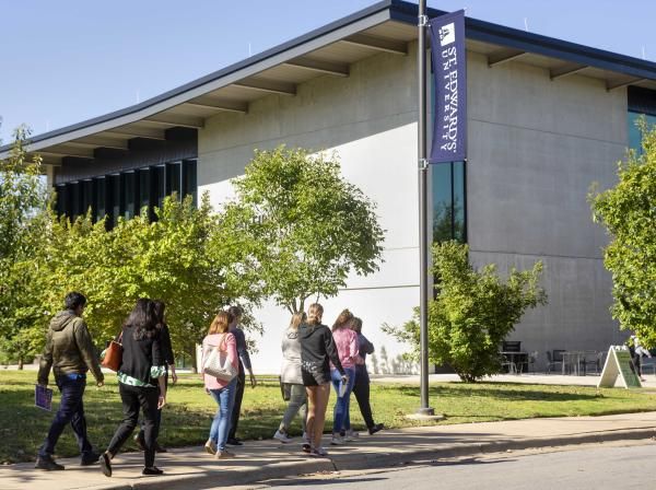 Families walk on a sidewalk in front of Munday Library during a campus tour.