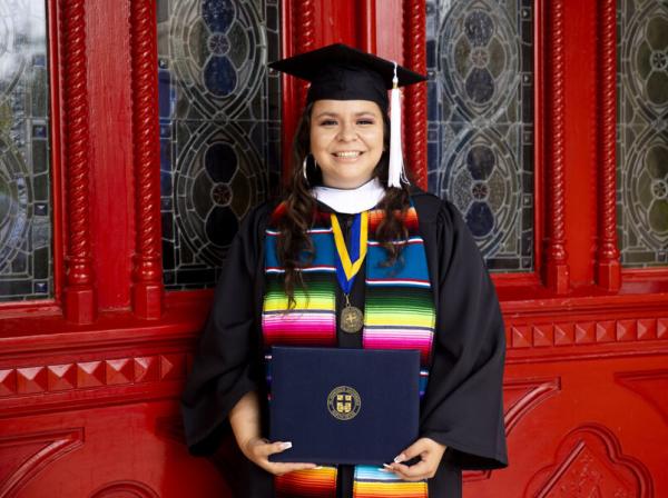 student holding diploma in front of red doors 