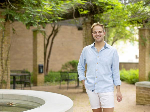 Bailey Galicia stands in the Moody Hall courtyard by a fountain with trees in the background.