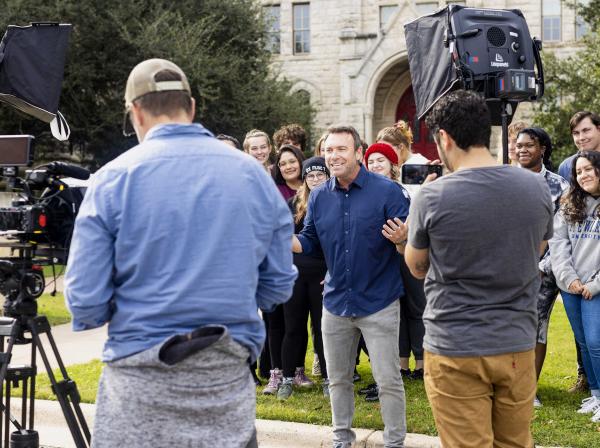 A film crew films Alex Boylan, host of The College Tour, as he speaks in front of a group of students outside of Main Building.