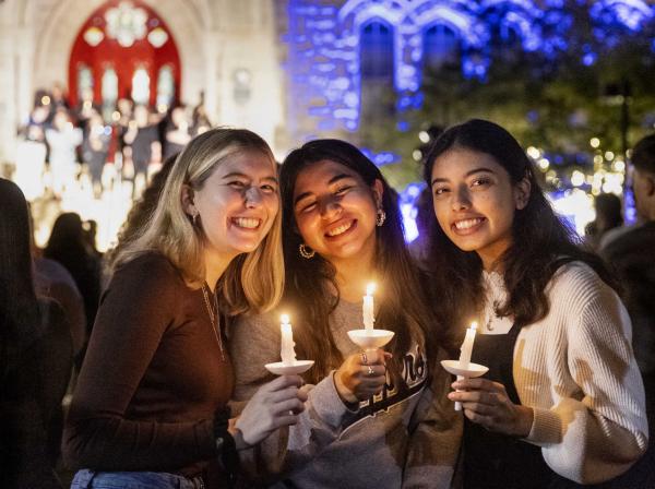 Three students stand in front of Main Building holding candles during Festival of Lights.