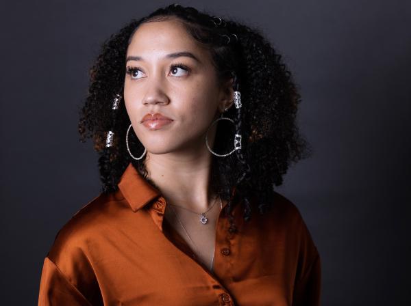 Alexis Reed wears a satin orange shirt and looks over her shoulder.