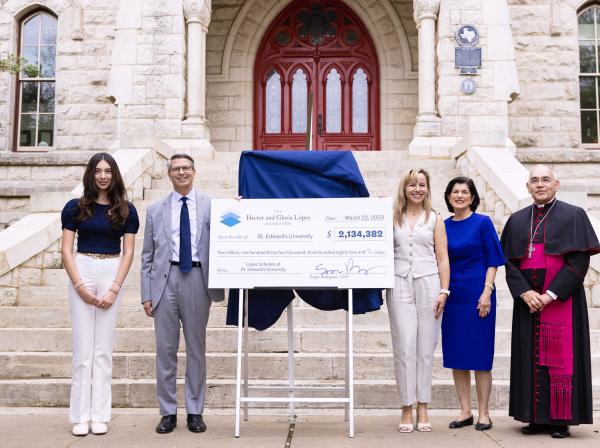 Five people stand with a large check on a stand at the steps of Main Building with the red doors in the background.