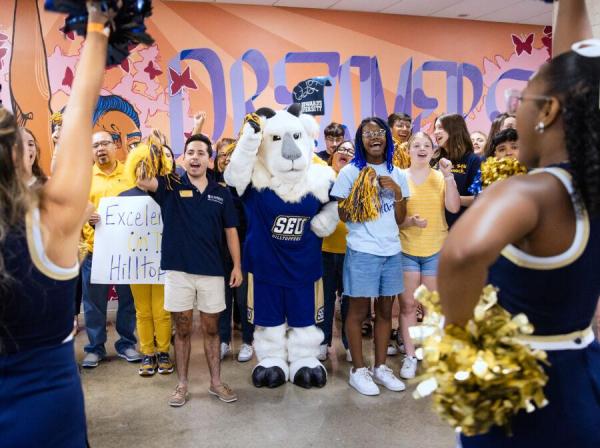 Cheerleaders frame a group of students and the Topper mascot as everyone cheers.