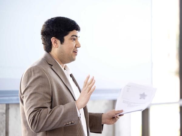 A person wearing a blazer holds papers and presents information.