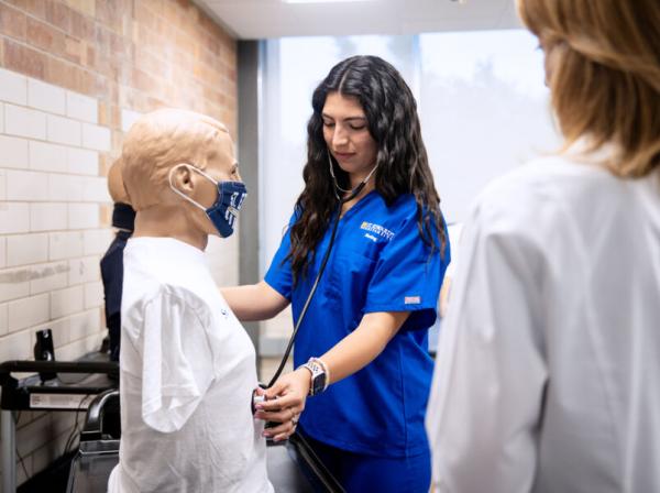 nursing student in blue scrubs learning in a nursing lab 