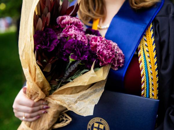 A detail of a graduate holding flowers and their degree.