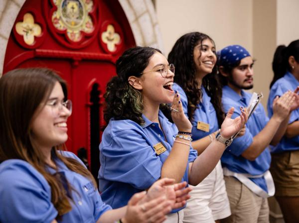 Five orientation leaders stand in matching blue polos and clap.