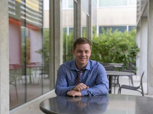 Professor Adam McCormick sits at a patio table outside of Equity Hall.