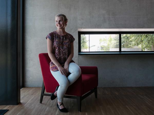 Alma Baker sits on a red chair and looks out the window in the Munday Library.