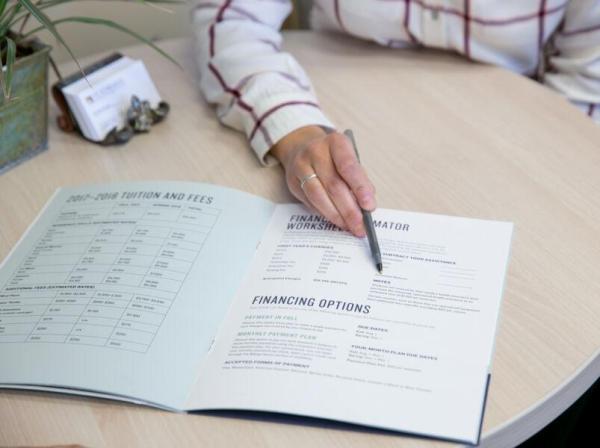 A person pointing at a financial aid pamphlet with a pen