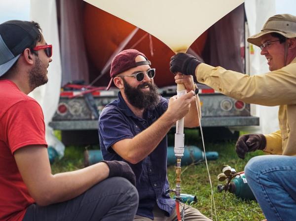 Three researchers kneel and work together to set up a weather balloon.