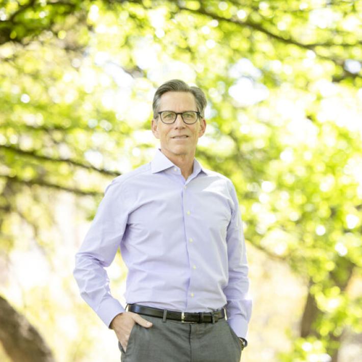 A man in glasses with a blue shirt posing underneath green leaves