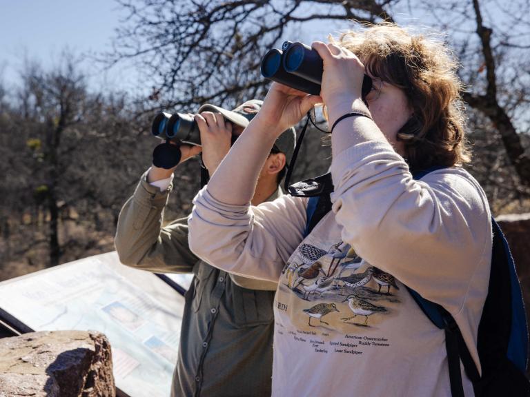 Two students on a school trip to Enchanted Rock for their Texas Ecology class hold up binoculars to study birds at a distance