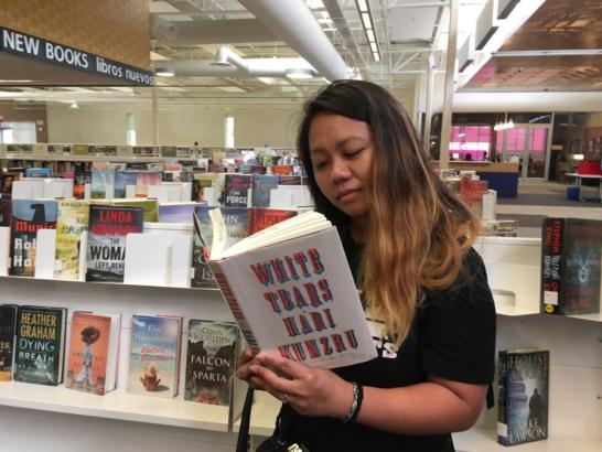 A student in a bookstore reading a book that says "White Tears by Hari Kunzru"