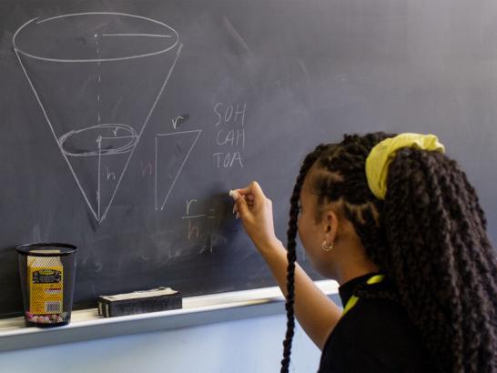 Student solving a math problem on the chalk board.