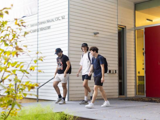 Three students smile as they walk and talk and exit the Campus Ministry building.