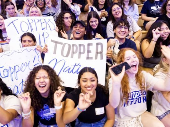 A crowd of students hold handmade spirit signs and cheer during a pep rally.