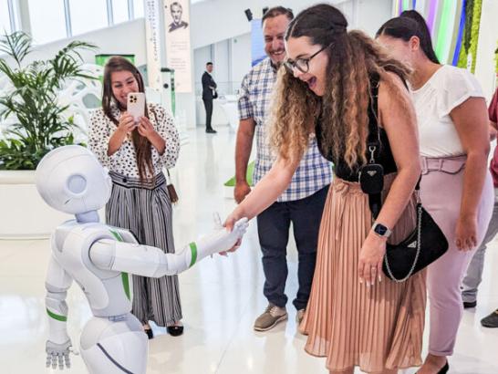 A student looks surprised while shaking hands with a robot. Another person takes a photo with their phone while a few others watch the interacrion.This is from a study abroad trip in Dubai.