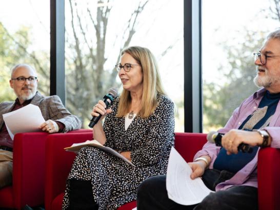 Three faculty members sit in red chairs in Munday Library on a panel discussion.