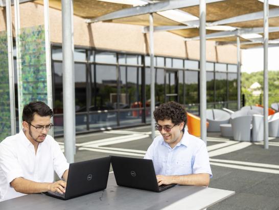 Two students sit on a modern patio and work on their laptops during their internships.