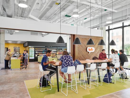 Students sit at a hightop table, hanging out and studying, while other students buy food items and interact with a cashier at the Grab and Goat.