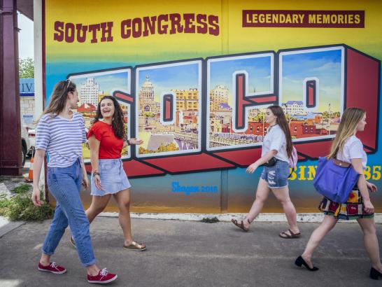 Students walk on South Congress Avenue past a colorful SoCo mural.